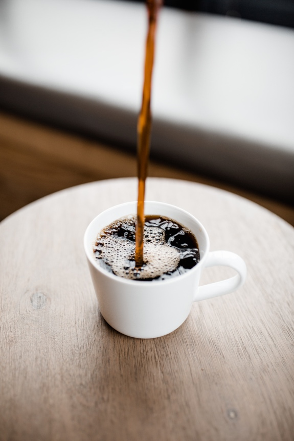 Black coffee is poured into a white cup.